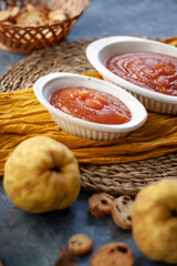 Homemade jelly quince in a white crockery containers with some quince fruits and little toasts to spread.