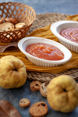Homemade jelly quince in a white crockery containers with some quince fruits and little toasts to spread.