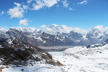 View of Everest mountain peak from the top of Renjo La Pass in Himalayas in sunny day. Everest rises above Lake Gokyo and the village of the same name. Clouds lies on the mountainside.