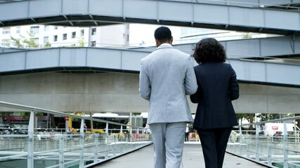 Back view of coworkers walking on street. Rear view of professional businessman and businesswoman walking near office building and discussing work together. Business concept
