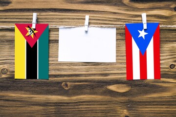 Hanging flags of Mozambique and Puerto Rico attached to rope with clothes pins with copy space on...