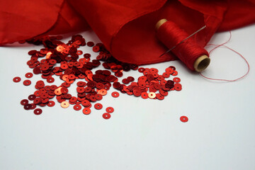 Red sequins, spool of red thread, needle on rippled red silk background.