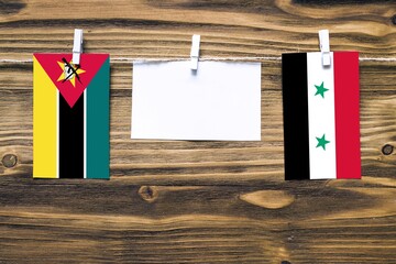 Hanging flags of Mozambique and Syria attached to rope with clothes pins with copy space on white...