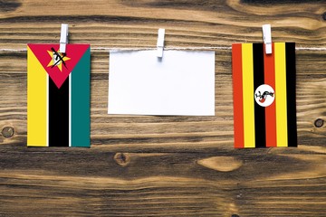 Hanging flags of Mozambique and Uganda attached to rope with clothes pins with copy space on white...