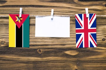 Hanging flags of Mozambique and United Kingdom attached to rope with clothes pins with copy space on white note paper on wooden background.Diplomatic relations between countries.