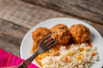 Mexican meatballs with red sauce and rice on wooden background