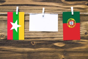 Hanging flags of Myanmar and Portugal attached to rope with clothes pins with copy space on white note paper on wooden background.Diplomatic relations between countries.