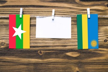 Hanging flags of Myanmar and Rwanda attached to rope with clothes pins with copy space on white note paper on wooden background.Diplomatic relations between countries.