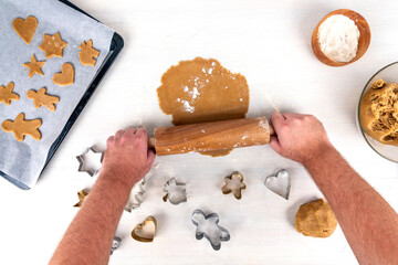Gingerbread baking concept with gingerbread dough, flour, rolling pin and gingerbread cookies on baking tray.  Hands holding rolling pin over dough.