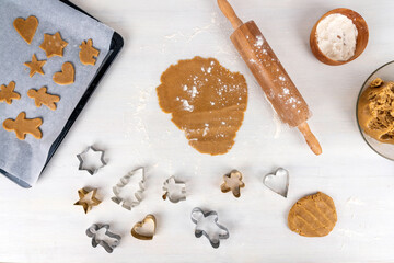 Gingerbread baking concept with gingerbread dough, flour, rolling pin and gingerbread cookies on baking tray.  Copy space for text on white kitchen table.