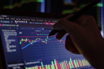 Closeup hand pointing pen on blue color monitor to analyze stock market graph