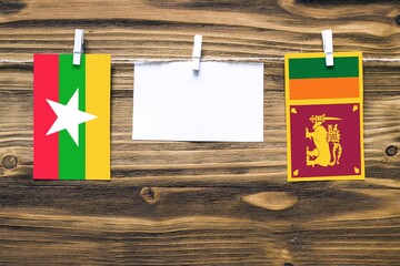 Hanging flags of Myanmar and Sri Lanka attached to rope with clothes pins with copy space on white note paper on wooden background.Diplomatic relations between countries.