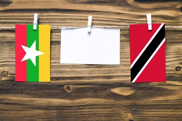 Hanging flags of Myanmar and Trinidad And Tobago attached to rope with clothes pins with copy space on white note paper on wooden background.Diplomatic relations between countries.