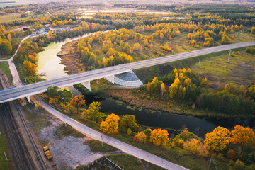 River bend autumn landscape with trees in orange colors and transport bridge. View from above