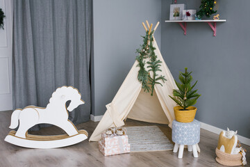 Rocking horse for children made of phoners and cardboard in a children's room decorated for Christmas or New Year, a wigwam tent for children and an artificial Christmas tree © Sunshine
