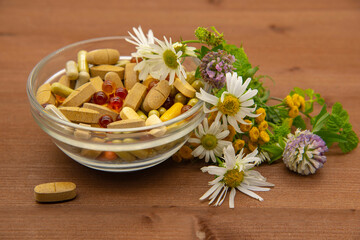 Obraz na płótnie Canvas A bowl with various capsules and tablets, medicinal and aromatic herbs.
