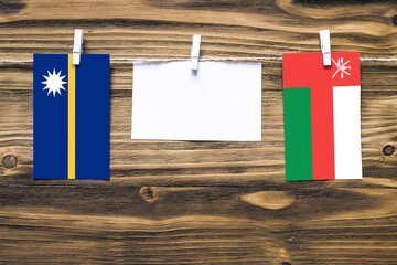 Hanging flags of Nauru and Oman attached to rope with clothes pins with copy space on white note paper on wooden background.Diplomatic relations between countries.