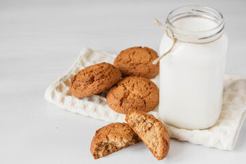 Milk in glass jar and oatmeal cookies near napkin on white table background. Copy, empty space for text