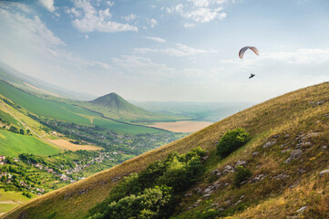 A paraglider flies in the sky in a cocoon suit on a paraglider over the Caucasian countryside with hills and mountains. Paragliding Sport Concept