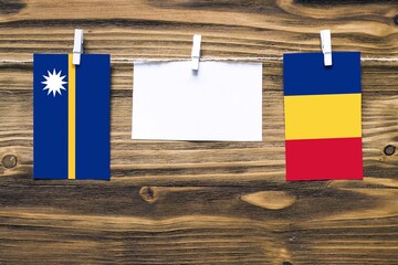 Hanging flags of Nauru and Romania attached to rope with clothes pins with copy space on white note paper on wooden background.Diplomatic relations between countries.