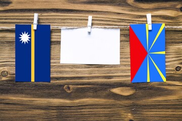 Hanging flags of Nauru and Reunion attached to rope with clothes pins with copy space on white note paper on wooden background.Diplomatic relations between countries.