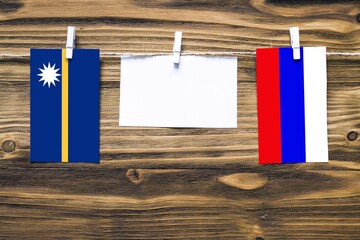Hanging flags of Nauru and Russia attached to rope with clothes pins with copy space on white note...