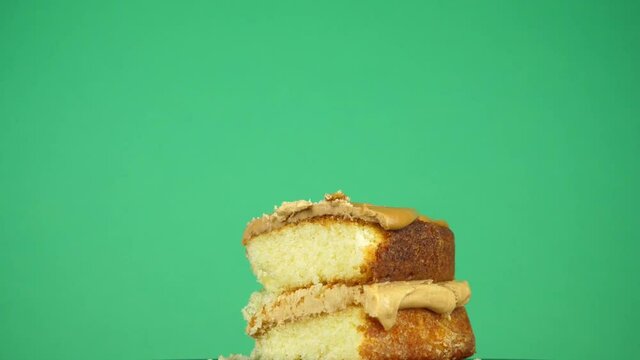 In front of a green studio backdrop, a slice of cake is picked up by a human hand