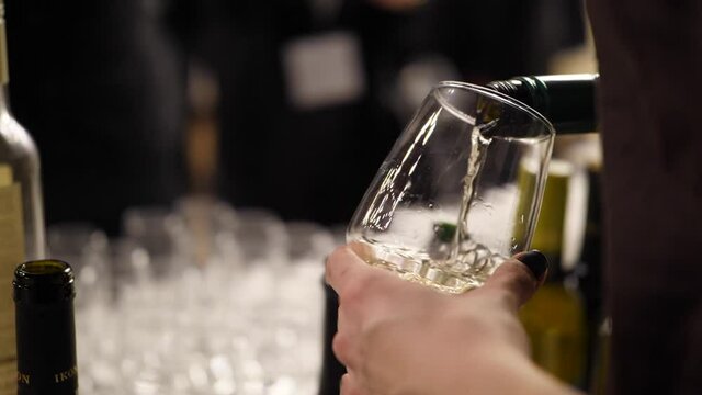 Waiter pouring white wine into wine glass at a wine tasting event. Close shot with the white wine splashing in the glass and forming beautiful bubbles.