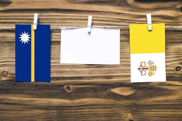 Hanging flags of Nauru and Vatican City attached to rope with clothes pins with copy space on white...