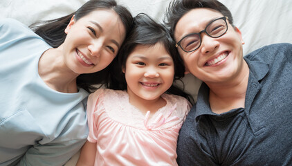 portrait of happy Asian family lying on bed and looking up and holding hands © saksit