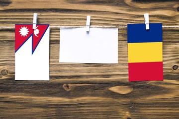 Hanging flags of Nepal and Romania attached to rope with clothes pins with copy space on white note paper on wooden background.Diplomatic relations between countries.