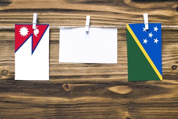 Hanging flags of Nepal and Solomon Islands attached to rope with clothes pins with copy space on...