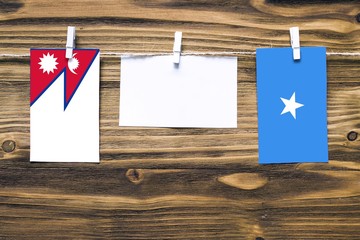 Hanging flags of Nepal and Somalia attached to rope with clothes pins with copy space on white note paper on wooden background.Diplomatic relations between countries.