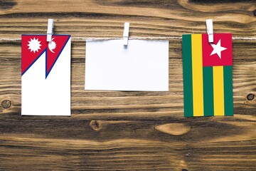 Hanging flags of Nepal and Togo attached to rope with clothes pins with copy space on white note paper on wooden background.Diplomatic relations between countries.
