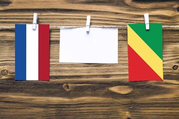 Hanging flags of Netherlands and Republic Of The Congo attached to rope with clothes pins with copy space on white note paper on wooden background.Diplomatic relations between countries.