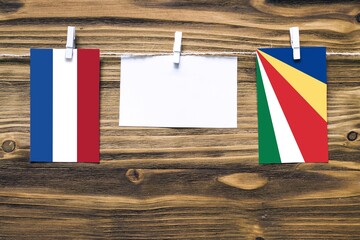 Hanging flags of Netherlands and Seychelles attached to rope with clothes pins with copy space on white note paper on wooden background.Diplomatic relations between countries.