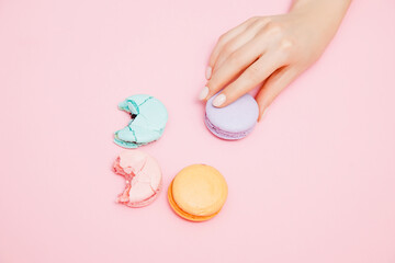 Bitten macaroons and woman hand with manicure on pink background, top view. Concept reducing...