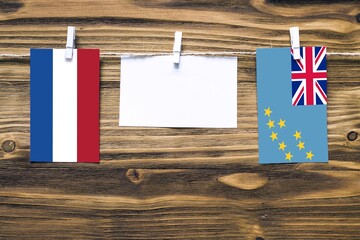 Hanging flags of Netherlands and Tuvalu attached to rope with clothes pins with copy space on white note paper on wooden background.Diplomatic relations between countries.