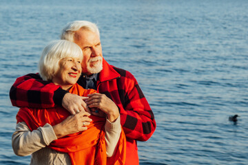 Fototapeta na wymiar cheerful senior citizens woman and man are standing and hugging on the lake, against the background of the bridge.