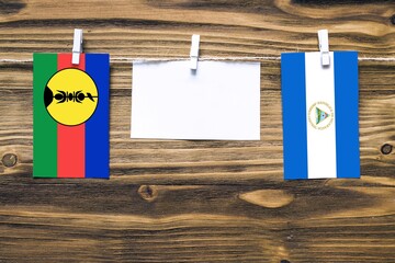Hanging flags of New Caledonia and Nicaragua attached to rope with clothes pins with copy space on...