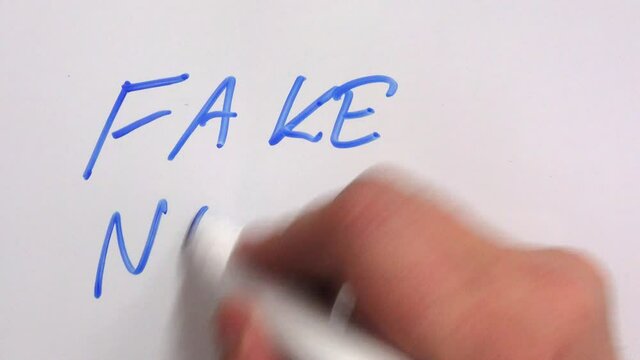 Man write "Fake news" to whiteboard with blue marker. After a while he erases a word fake.