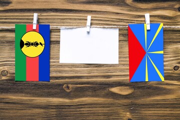 Hanging flags of New Caledonia and Reunion attached to rope with clothes pins with copy space on...