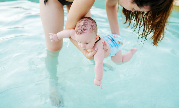 Insecure Caucasian 6 months old baby boy learning how to swim at swimming pool. Mother holding her son. First time at pool concept.