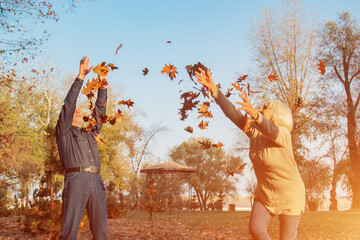 Elderly couple happily throws autumn fall leaves sitting in a park. Positive emotions of the elderly.
