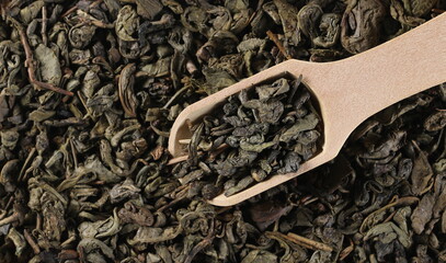 Dry green tea leaves in wooden scoop background, top view