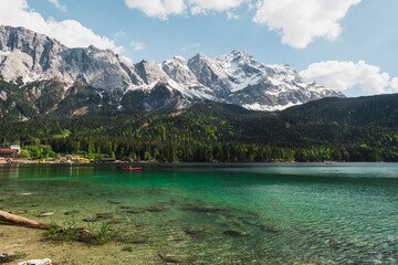 Bavarian Eibsee lake at the foot of snow-covered Zugspitze with clear azure water, white clouds and blue sky during summer (Grainau, Germany, Europe)
