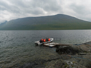 group of tourist hikers on motor boat at pier prepar to crossing Teusajaure lake at Kungsleden hiking trail. Lapland mountains nature landscape in summer, moody sky.