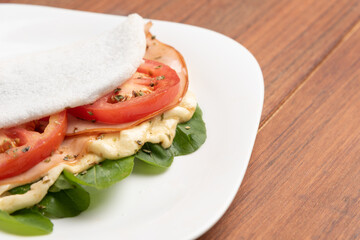 Tapioca filled with ham, cheese and tomato, on wooden background. Flatbread made from cassava (also known as casabe, bammy, beiju, bob, biju).