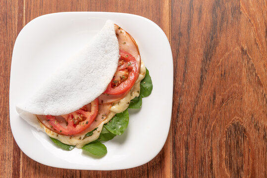 Tapioca filled with ham, cheese and tomato, on wooden background. Flatbread made from cassava (also known as casabe, bammy, beiju, bob, biju).