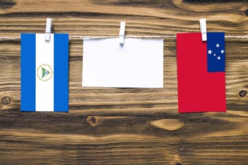 Hanging flags of Nicaragua and Samoa attached to rope with clothes pins with copy space on white note paper on wooden background.Diplomatic relations between countries.